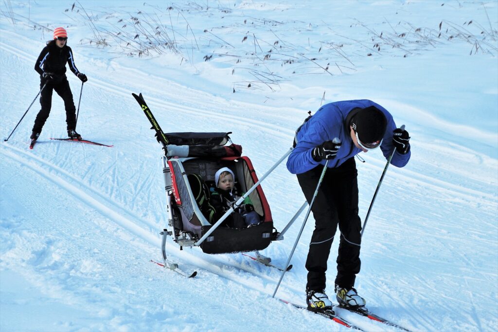 Skiurlaub Vater Mutter Kind Kinderwagen Anhänger Ski Skiurlaub mit der Familie planen – Tipps für stressfreie Winterferien